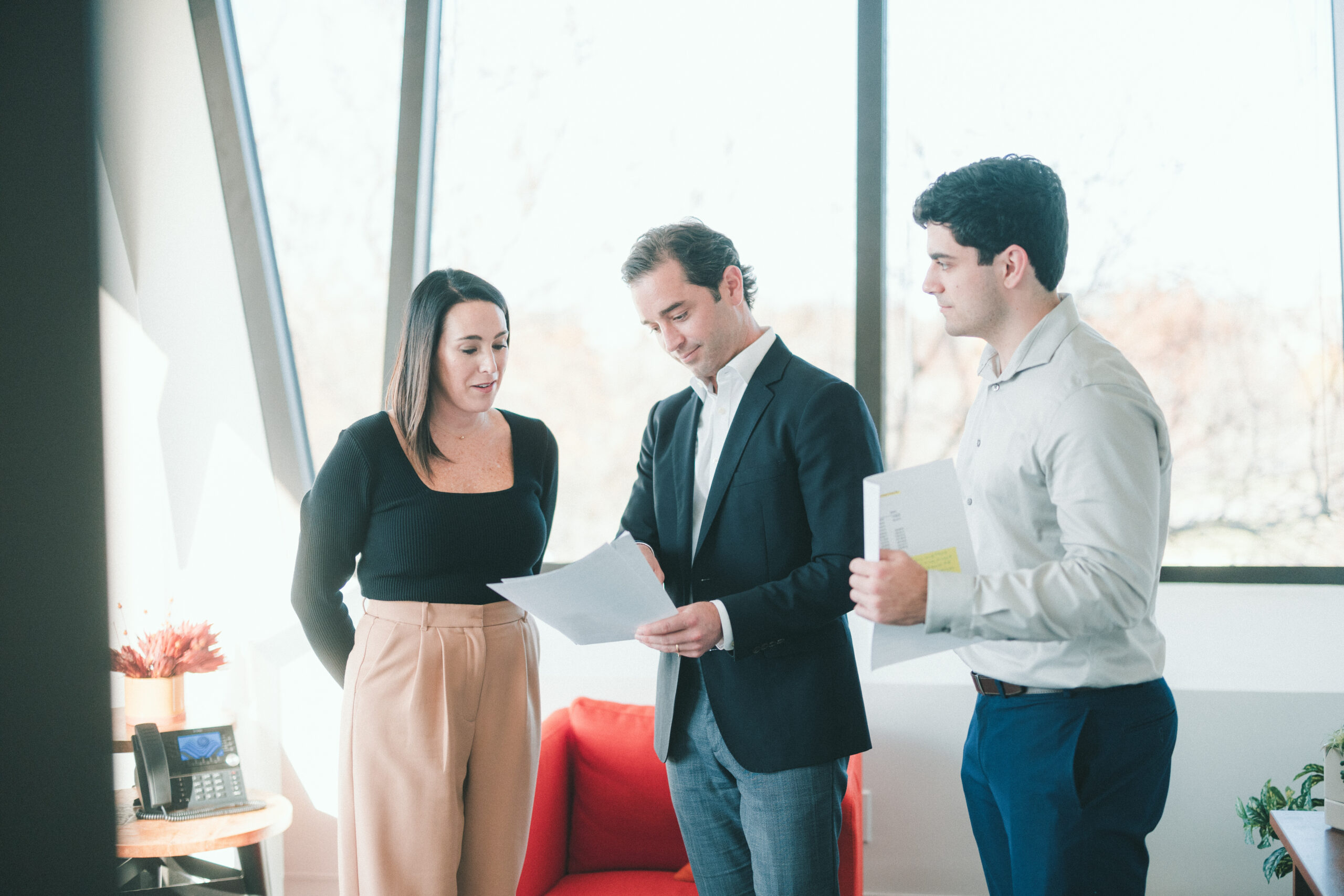 Two professional Men and One Professional woman standing talking about a sheet of paper